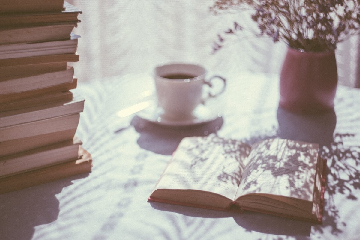 šoljica kafe i naslagane knjige na stolu